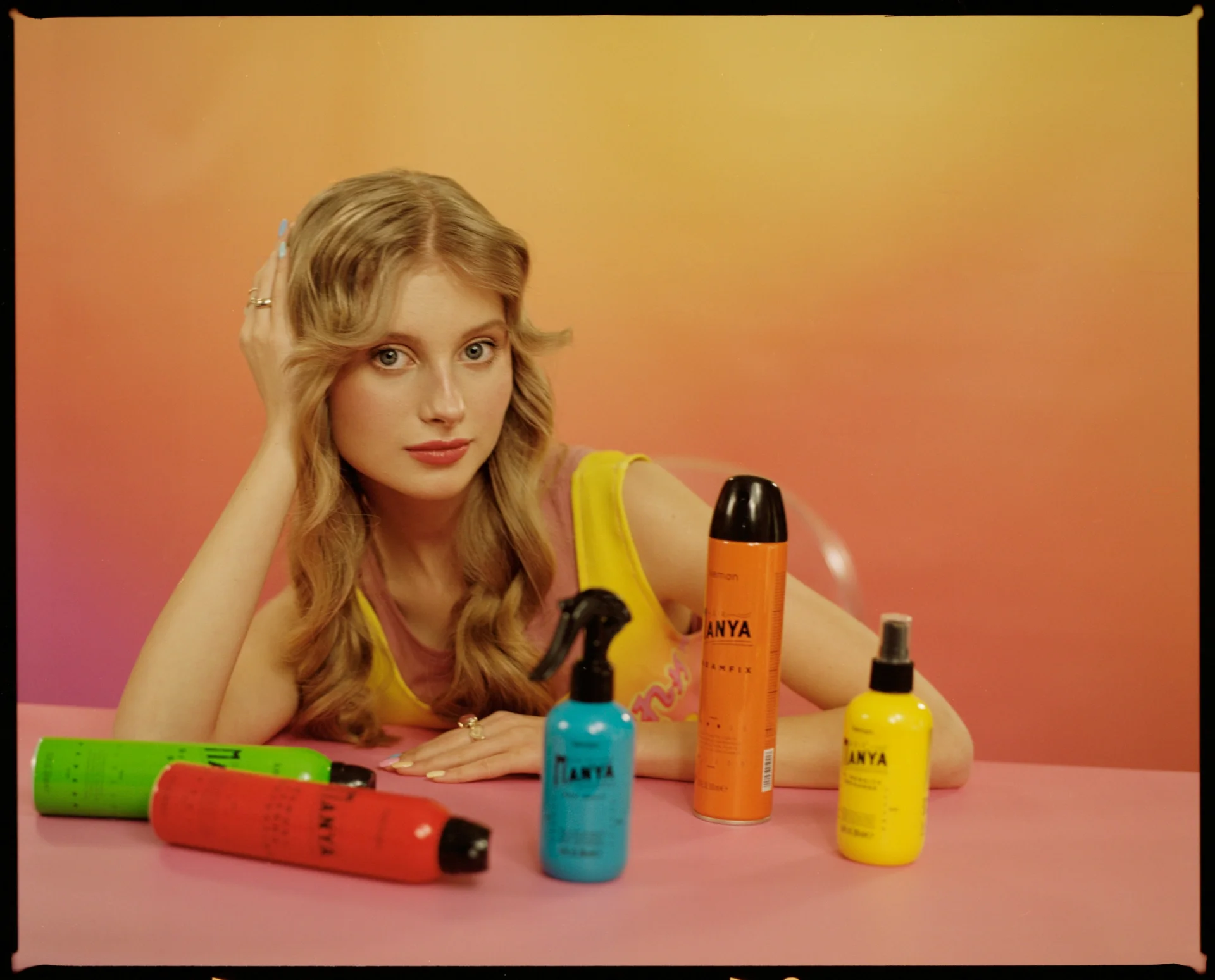 Blondynka pozuje z kolorowymi butelkami produktów do włosów, trzymając je w dłoniach.