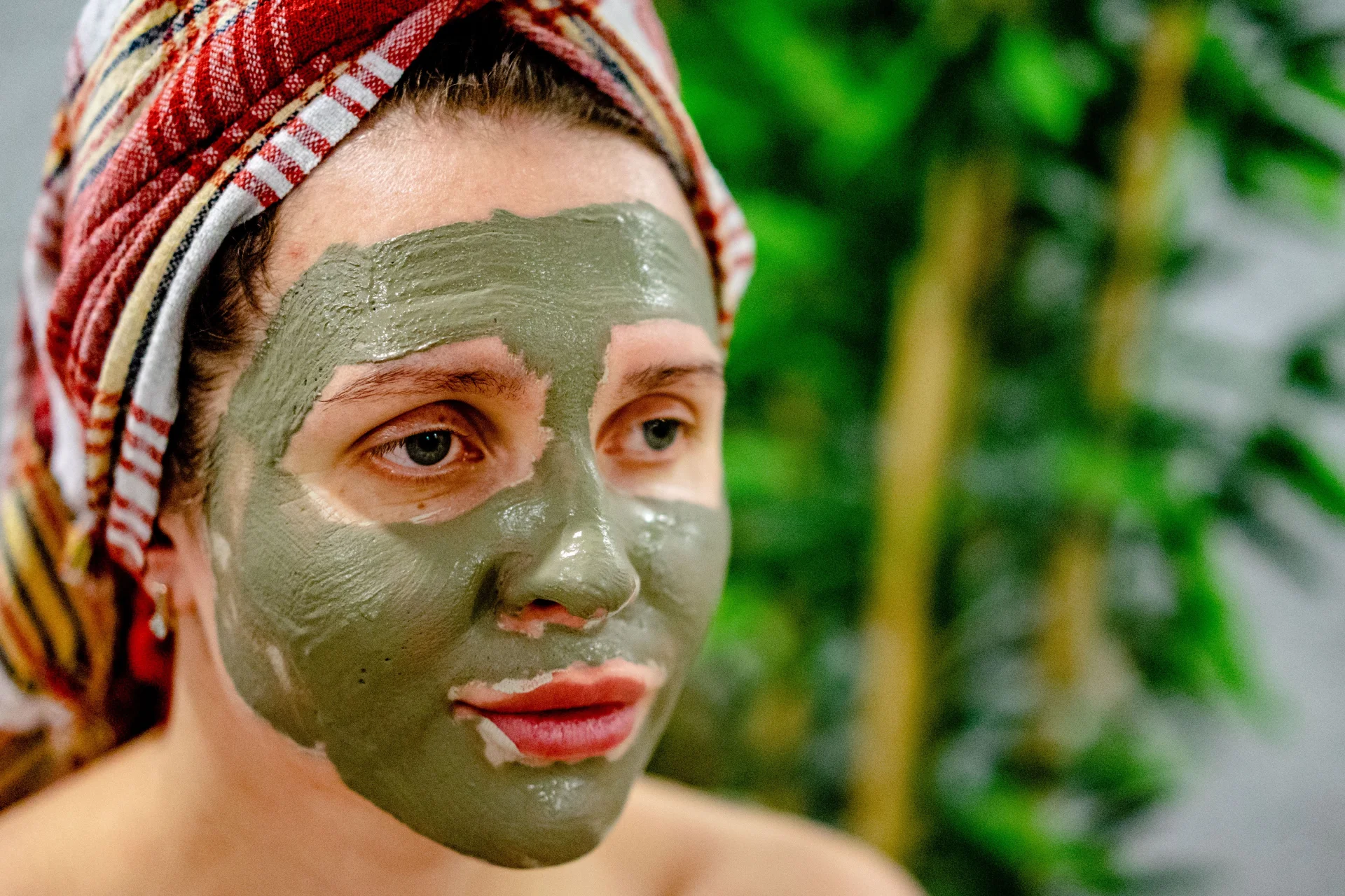 Kobieta z maską błotną na twarzy, z zamkniętymi oczami, zrelaksowana podczas zabiegu spa.